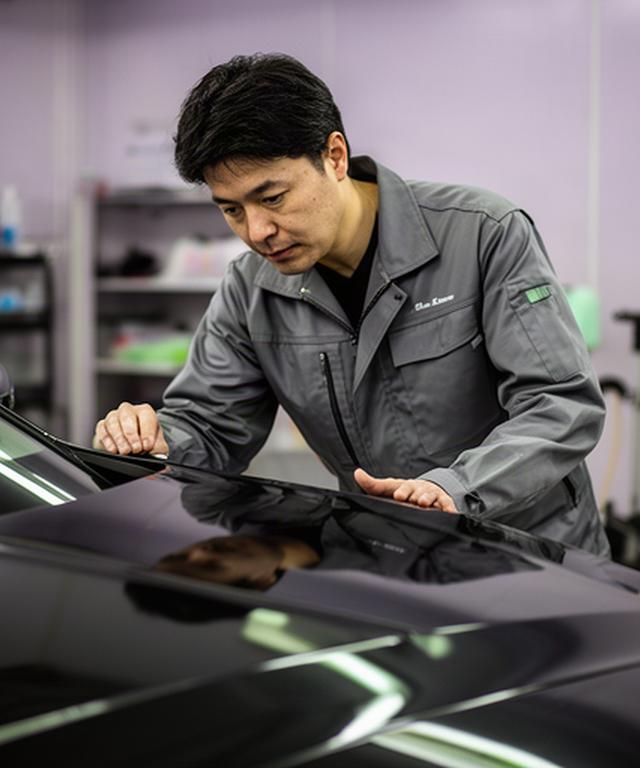 宜野湾の屋内施工ブースで高級車の塗装を確認する専任技術者