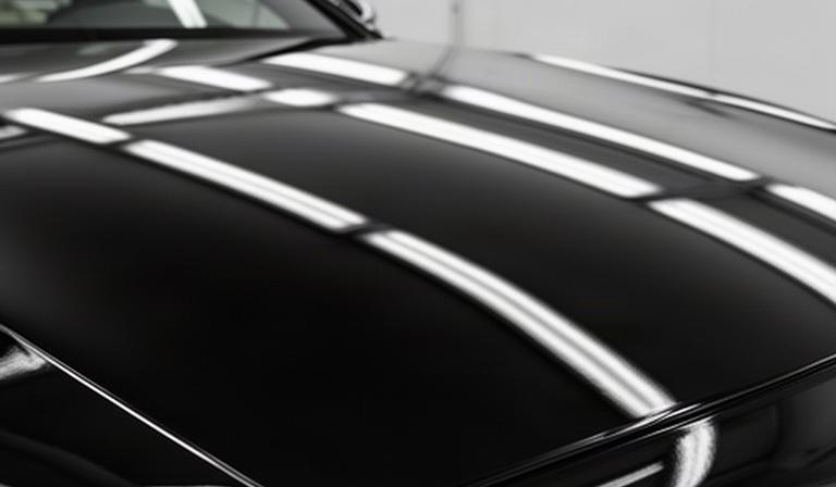 照明の下で艶を取り戻した黒い高級車のボンネットの塗装面